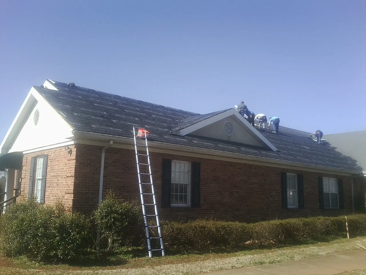 Crew tearing shingles off a brick ranch roof with a ladder set — Emergency Roof Repair work by our crew in Ohiopyle