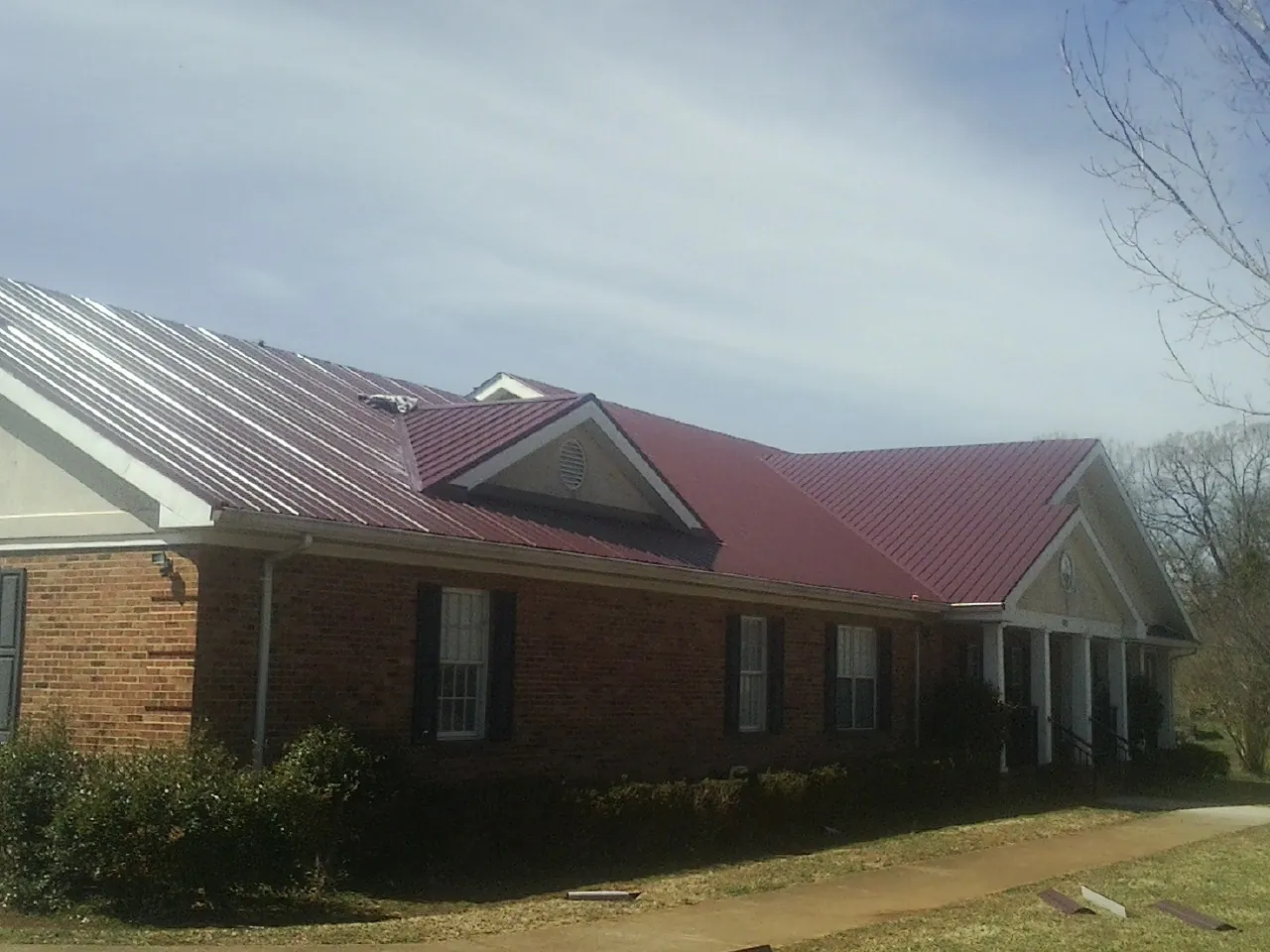 Red metal roof with gabled entries on a long brick building, from a Hail Damage Roof Repair job in Ohiopyle