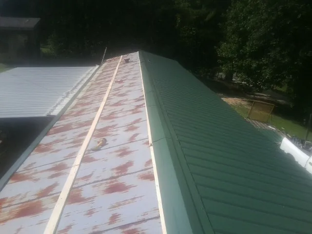 Old rusted panels beside newly installed green metal roofing — Wind Damage Roof Repair by Roofing Brothers in Ohiopyle