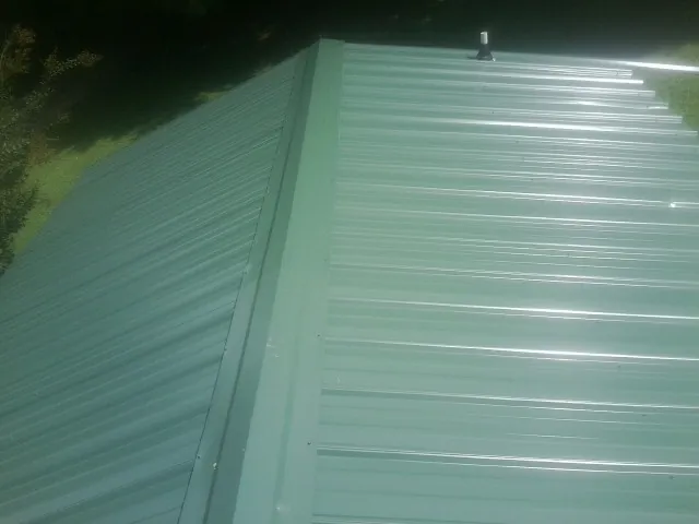 New green metal panels meeting at the ridge of a roof — Flat Roof Repair work by our crew in Ohiopyle
