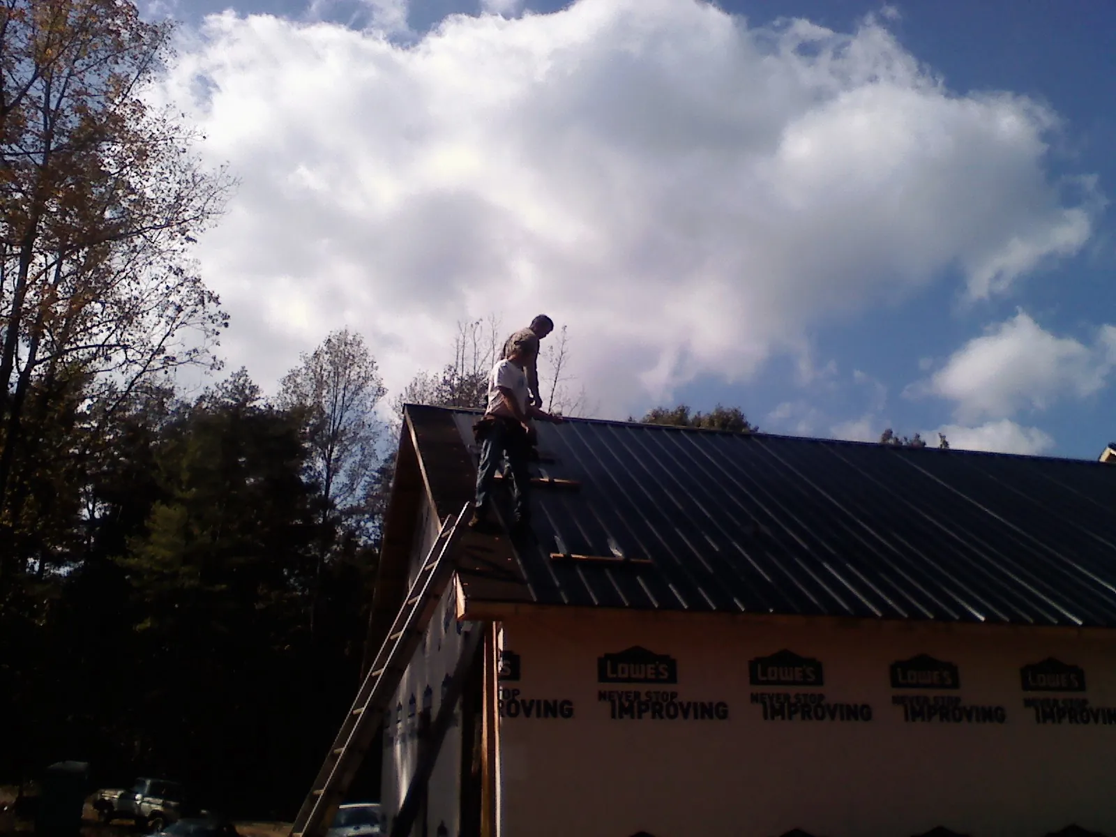 Roofer fastening dark metal panels high against a cloudy sky, from a Roof Inspection job in Ohiopyle