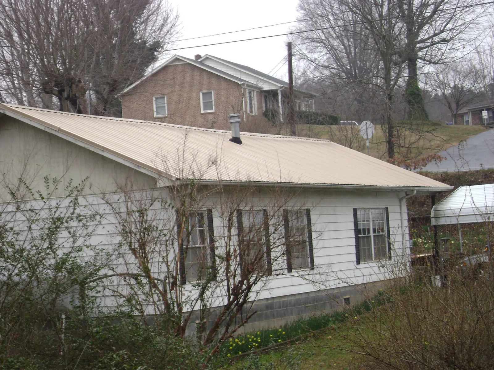 Tan metal roof on a white sided house set into a hillside — Commercial Roofing by Roofing Brothers in Ohiopyle