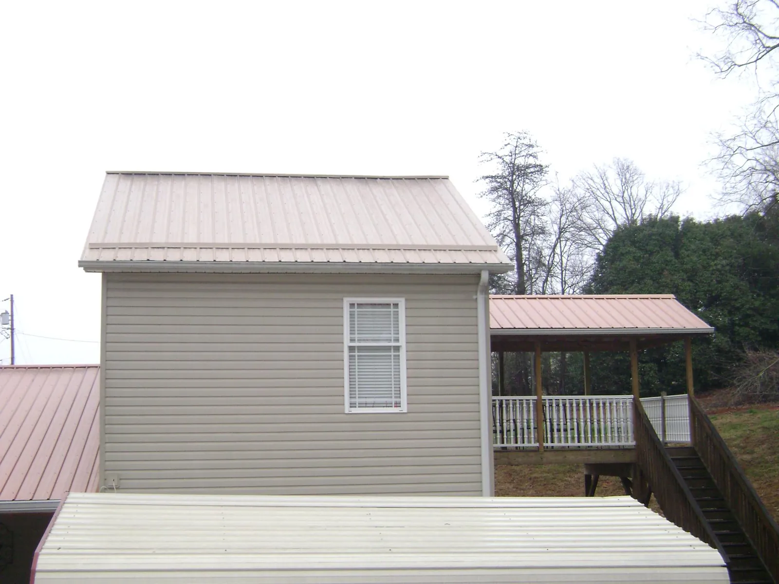 Tan metal roofs on a two story addition and attached porch, from a Roof Replacement job in Ohiopyle